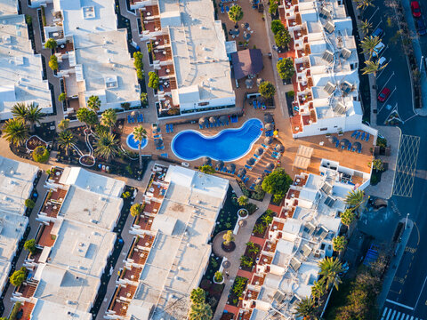 Aerial view of a vibrant blue pool nestled among the white buildings, palm trees, and pathways, creating a stunning contrast, Playa Blanca, Lanzarote, Canary Islands.