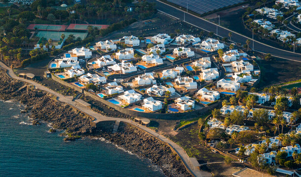 Aerial view of white villas clustered near the dark, rocky coastline, where the deep blue sea meets the volcanic shore, Playa Blanca, Lanzarote, Canary Islands.