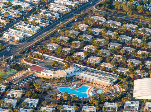 Aerial view of the azure pool reflecting the sky, surrounded by the terracotta roofs of the resort and the lush green palm trees, Playa Blanca, Lanzarote, Canary Islands.