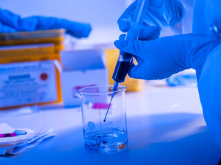 Fototapeta premium Alternative angle of syringe and beaker laboratory procedure with blue dramatic lighting capturing analytical chemistry process
