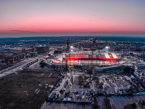 Aerial view of a vibrant stadium glowing with bright red and white lights against the dusky sky, Frisco, Texas, United States.