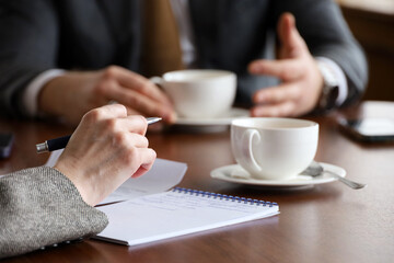 People talking at the table with tea cups, woman with pen and man in business suit. Concept of business meeting, discussion, interview © Oleg