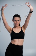 Woman in sportswear holding a tape measure above her head, symbolizing weight loss progress,...