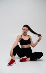 Fototapeta premium Young fitness woman in black sports bra and leggings sitting on a studio floor, pausing from workout with strong body language, focusing on wellness and healthy lifestyle
