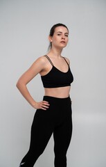 Fototapeta premium Young woman standing confidently in black athletic wear, showcasing fitness and a healthy body, promoting an active and wellness-focused lifestyle against a clean, light studio backdrop
