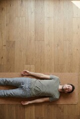 Man lying in Savasana pose on yoga mat in bright, minimalist studio for relaxation and mindfulness practice