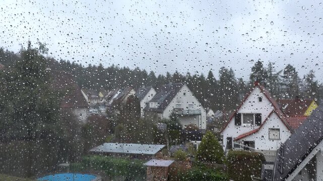 Ein mit Regentropfen benetztes Fenster an einem regnerischen Tag mit Blick auf ein Wohngebiet