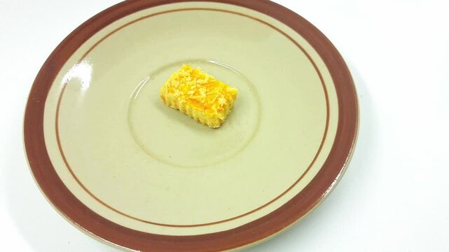 Small rectangular piece of fried yellow battered food rests in the center of a beige and brown rimmed ceramic plate against a white background.