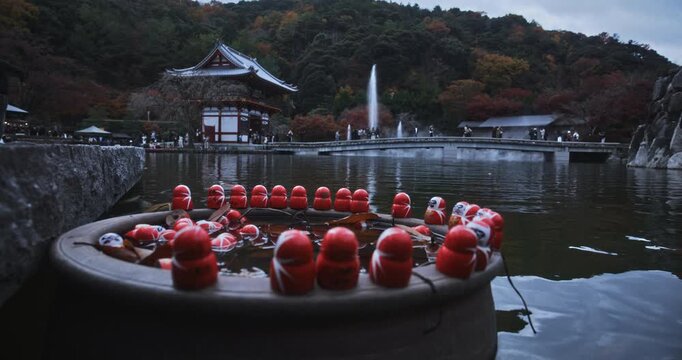 Tiny daruma dolls in a circle on pond surface near beautiful shrine in Japan