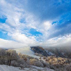 winter mountain ridge with snowbound forest below in dense mist and clouds