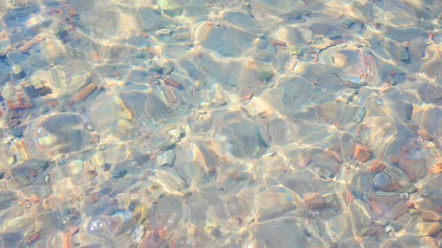 Calm ripples on the crystal water surface of a pebble beach. Sunny day.