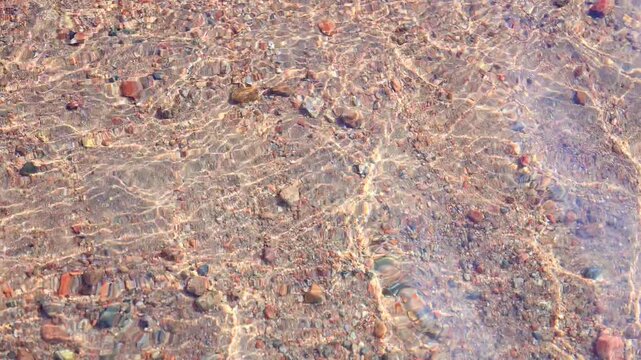 Calm ripples on the crystal water surface of a pebble beach. Sunny day.
