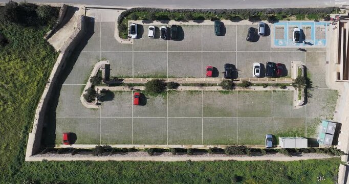 Aerial view of a car park with cars, set against the backdrop of green grass and a building, creating a colorful contrast, Gharb, Ta' Pinu Cathedral, Malta.