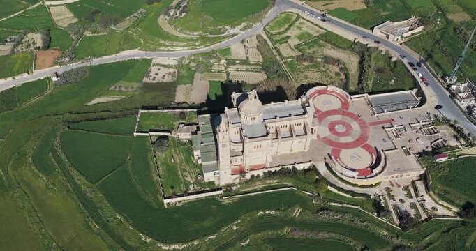 Aerial view of the Ta' Pinu Cathedral surrounded by lush green fields contrasting with the pale stone of the church, Gharb, Ta' Pinu Cathedral, Malta.