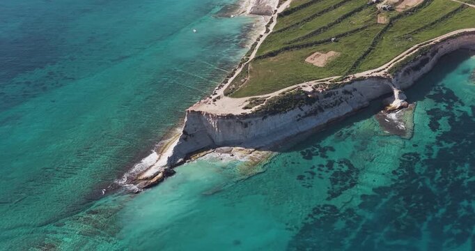Aerial view of the rugged coastal cliffs meeting the turquoise sea, creating a stunning contrast in colors and textures, Munxar Path, Marsaskala, Malta.