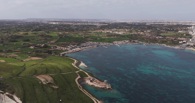 Aerial view of Munxar Path's contrasting turquoise waters meeting the rugged coastline and verdant landscape, Marsaskala, Malta.