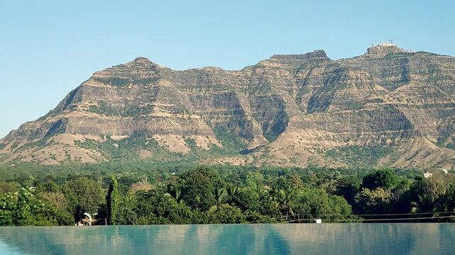 Pavagadh hill mountain behind luxury resort pool Gujarat India. Calm blue swimming pool reflects rocky plateau and green forest, peaceful travel and vacation destination in western India..