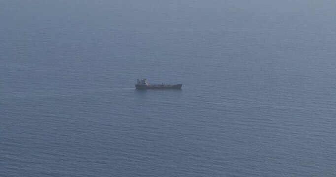 Aerial view of a ship sailing in the middle of the ocean, its dark silhouette contrasting with the shimmering blue water, Munxar Path, Marsaskala, Malta.