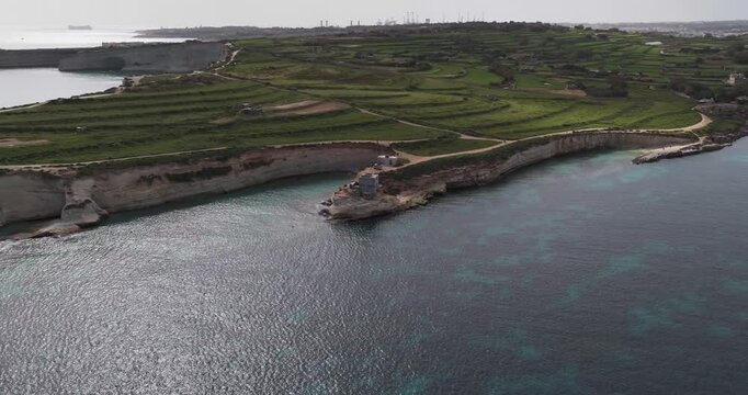 Aerial view of the dramatic coastline with white cliffs contrasting with the deep blue sea, alongside vibrant green terraced fields, Munxar Path, Marsaskala, Malta.