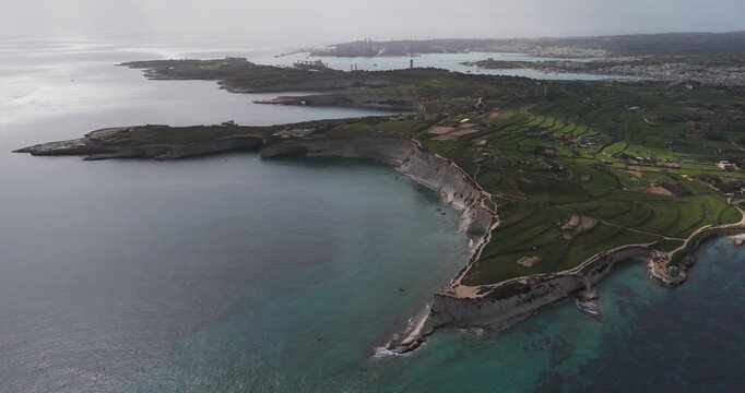 Aerial view of the rugged coastline with green fields and turquoise waters meeting the rocky shores, Munxar Path, Marsaskala, Malta.