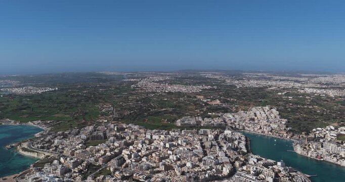 Aerial view of the cityscape where buildings meet turquoise waters, showcasing a vibrant contrast between urban development and natural beauty, Marsaskala, Malta.
