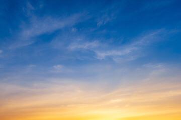 Obraz premium Dramatic sunset sky with orange and blue gradient clouds background,A beautiful panoramic view of the twilight sky during sunset, featuring soft wispy clouds illuminated by golden light against.