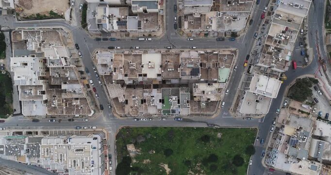 Aerial view of dense buildings, roads filled with cars, and patch of green space create a textured urban landscape from above, Mellieha, Malta.