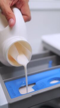 Close up of a hand pouring liquid fabric softener into the dispenser drawer of a washing machine. Laundry day and housekeeping concept. Vertical Shot.