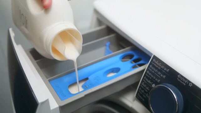 Close up of a hand pouring liquid fabric softener into the dispenser drawer of a washing machine. Laundry day and housekeeping concept.