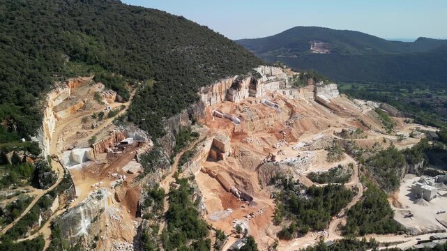 Drone panorama over controlled blasting that splits a massive bench slab at the Botticino marble quarry. Video showing the scale of extraction of this famous marble in Brescia, Italy