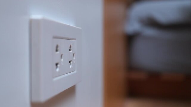 Close up of woman a hand unconnected a white power adapter to a wall socket. Concept of charging devices and electricity consumption.