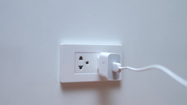 Close up of woman a hand connecting a white power adapter to a wall socket. Concept of charging devices and electricity consumption.