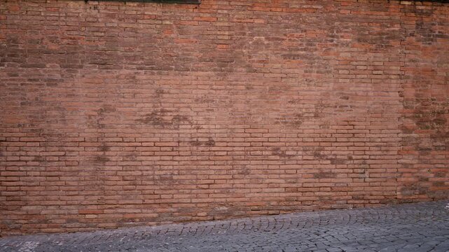 Weathered red brick wall texture with cobblestone pavement foreground, finely detailed and sharp street background; background backplate copyspace.