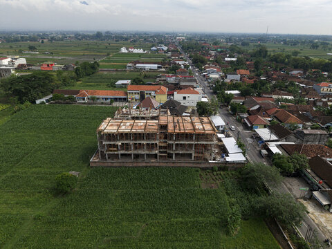 Aerial view of a building under construction amid lush green fields and a road lined with trees, Klaten Regency, Central Java, Indonesia.