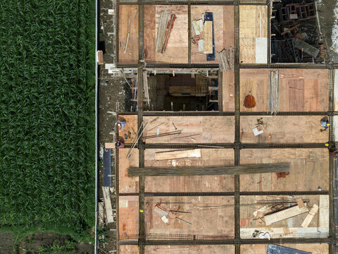 Aerial view of a building under construction adjacent to a lush green field, a stark contrast of raw wood and vibrant nature, Klaten Regency, Central Java, Indonesia.