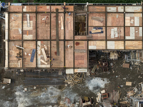 Aerial view of the unfinished building with the grid wooden frame and plywood, surrounded by debris and muddy ground, Klaten Regency, Central Java, Indonesia.