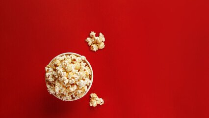 Top view of popcorn bucket and scattered kernels on red surface. Food flat lay concept.