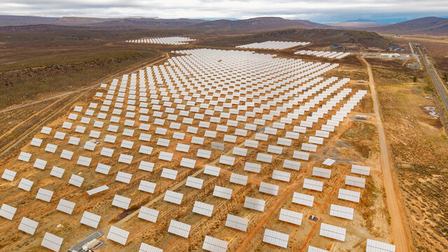 Aerial view of rows of solar panels glinting under the sky, reflecting the vast energy landscape, stretching across the arid terrain, Touws River, Western Cape, South Africa.