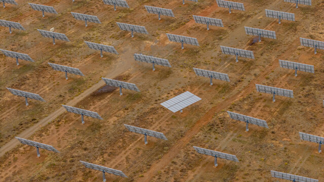 Aerial view of a solar farm with repetitive, geometric patterns across the arid landscape, contrasting metallic panels against the warm earth tones, Touws River, Western Cape, South Africa.
