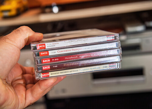Paris, France - Sep 9, 2025: Closeup of a hand holding a stacked selection of Capriccio label SACD classical albums in a home audio setting with warm background equipment visible