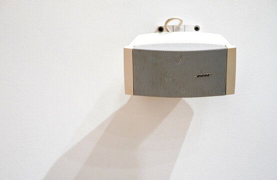 Paris, France - Dec 12, 2022: A white Bose wall-mounted speaker casts a long soft shadow across a textured light wall, creating a clean minimalist composition with subtle indoor lighting