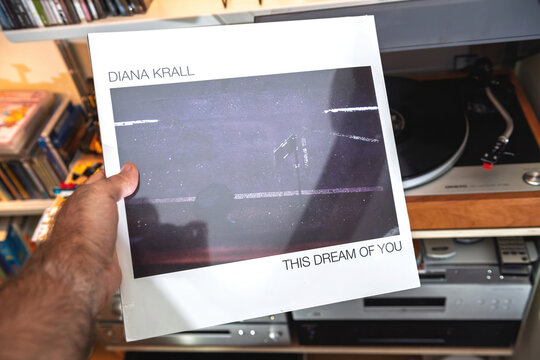 Paris, France - Sep 9, 2025: A hand presents the Diana Krall This Dream of You audiophile LP in its shrink wrap, held above a turntable and shelves in a warm home listening setup