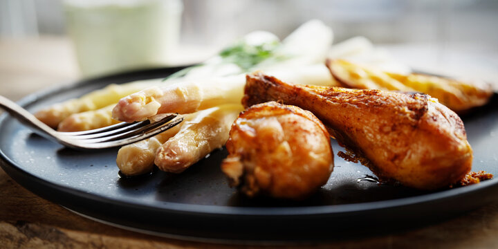 Black ceramic plate of roasted white asparagus and crispy chicken drumsticks. Healthy food for a spring diet. Close-up.