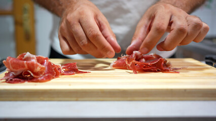 Closeup of chef handling meat. Professional chef skillfully prepares thin slices of cured meat