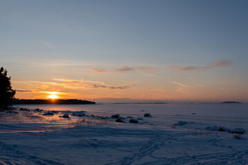 Obraz premium Winter sunset over a frozen sea with snow-covered shore and distant islands