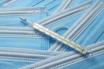Close-up of a mercury thermometer and a stack of blue medical masks