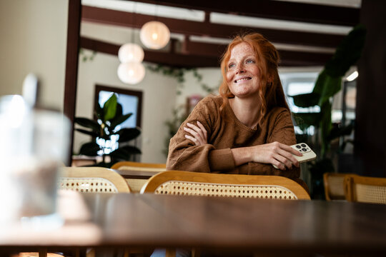 Small business owner sitting in cafe with mobile phone smiling
