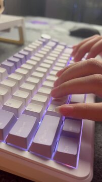 Close up of hands typing on a white mechanical keyboard with purple RGB backlit and purple keycaps.