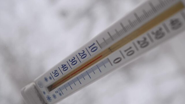 Outdoor thermometer shows a temperature of minus fifteen degrees Celsius. Close-up shot with a shallow depth of field and a blurry, snowy background.