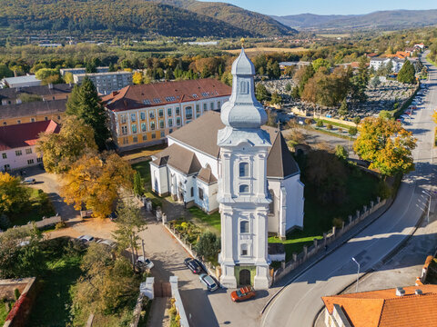 Aerial view of the Cathedral of the Assumption of the Blessed Virgin Mary, its white facade rising majestically against the backdrop of autumn trees, Roznava, Kosice Region, Slovakia.
